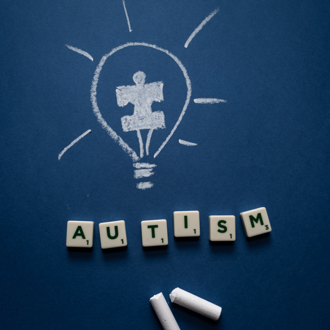 Autism spelt with scrabble tiles, on a navy blue background with chalk and a drawn picture of a light bulb